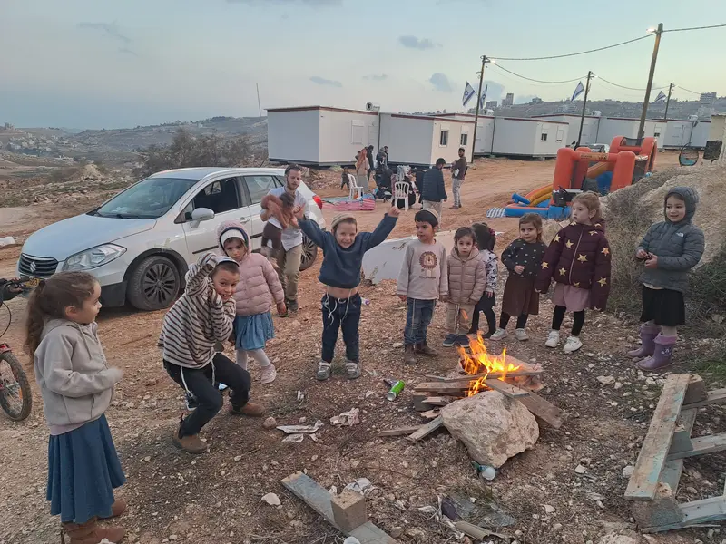 מדורה קהילתית עם ילדים רבים, רכבים וקרוואנים סביב
