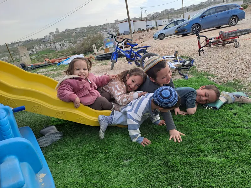 פעוטות על מגלשה בדשא, אופניים ונוף גבעות ברקע